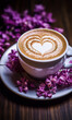 Cup of coffee with heart-shaped foam and purple flowers on wooden table