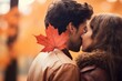 A couple shares a kiss behind a maple leaf in autumn.