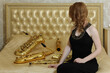 Woman in black dress sits with sax on bed with wind instruments in studio