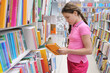 Girl with braids chooses book in large bookstore in shopping center