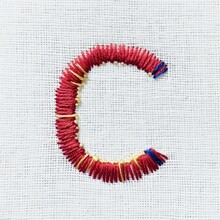 A close up of a red bracelet on a white cloth, embroidery on white background