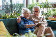 © pikselstock - Happy senior couple using digital tablet while sitting on sofa in living room