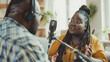 © Sabrina - African people having fun talking on microphone inside studio while streaming online podcast - Black male host doing interview with curvy woman - Models by AI generative