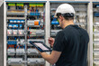 © puhimec - Man, an electrical working in a switchboard with fuses, uses a tablet.
