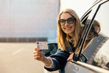Fototapeta Mapy - happy young woman showing her new driver license out of car window after successful test at driving school. copy space