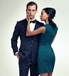 © ArcursJointTeam/peopleimages.com - Portrait, man and woman in elegant fashion in studio and confidence in vintage style in mock up. Face, pride or young for interracial couple in formal clothes and touch for care by white background