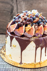 Wall Mural - Beautiful cake with figs dipped into melted chocolate, pecan nuts, grapes, chocolate bites and cookies on the top on rustic background