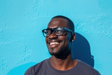 Wall Mural - black man wearing glasses smiling and talking against blue background