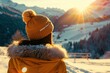 winter girl in winter hat looking at snowy mountains sun over background