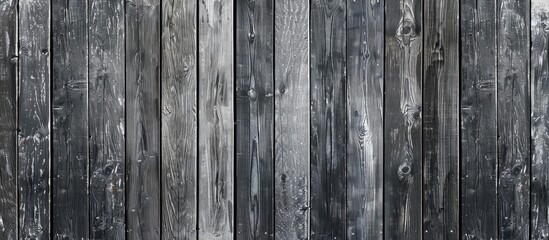 A monochrome photograph capturing the intricate pattern of a wooden fence among the natural landscape of a woodland. The grey tones create a striking contrast against the green grass