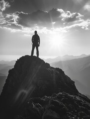 Sticker - Man stands on mountain peak, looking out at horizon. Sky is cloudy, but sun is shining brightly, creating beautiful contrast between light and darkness