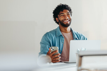 Happy young business man sitting with smartphone and laptop at desk