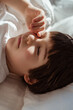 Close-up portrait of cute little toddler boy lying on bed waking up at sunny morning. Light and shadows from sunlight