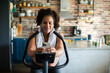 © Davor - Young pregnant latina woman exercising on an indoor bike and using a smartphone