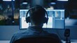© Christiankhs - Rear view of a young man in headphones listening to music while working on a computer at night