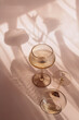 Two glasses with white wine placed on light beige background with shadows
