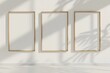 Drei Rahmen im A4-Format stehen nebeneinander auf einer weißen Wand, drei leere Poster, helle Holzrahmen, viel Sonnenlicht
