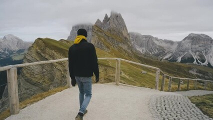 Wall Mural - Man traveler stands on the observation deck in the national park of mountain Seceda in the Dolomites. Alps mountains in autumn or winter. Beautiful alpine mountains in Italy. Seceda, one of the most