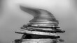 a black and white photo of a wooden staircase in the middle of a foggy area with a bench on the bottom of it.