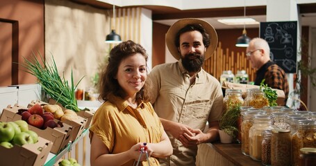 Canvas Print - Portrait of happy vegan couple buying pantry staples from zero waste supermarket. Smiling clients shopping for bulk food products in reusable jars from local neighborhood store, zoom in shot