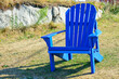 © Dolores  Harvey - A vibrant empty royal blue color Adirondack chair in a lush green grassy garden. There's a rock or boulder-style wall behind the outdoor plastic furniture. The chair has a curved back with slats.