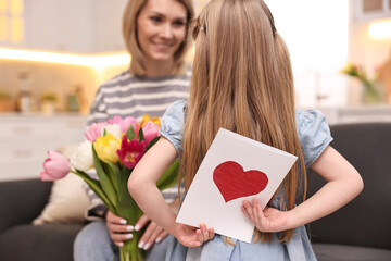 Canvas Print - Little girl hiding greeting card for mom at home, selective focus. Happy Mother's Day