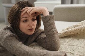 Canvas Print - Sad young woman sitting near sofa at home, space for text