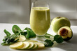 A glass of green juice is on a table with a sliced apple and spinach