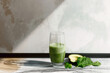 A glass of green juice with a slice of avocado and spinach on a table