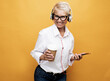 senior woman with short hair listening to music with headphones and holding takeaway coffee