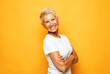 beautiful senior woman with short hair with crossed arms over yellow background.