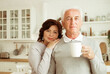 elderly couple drinking coffee in the kitchen while sitting at the table.