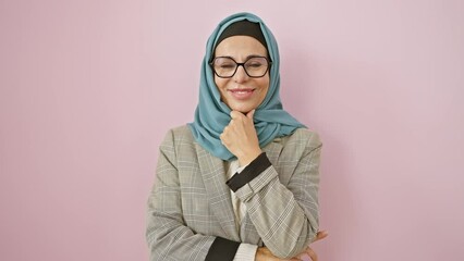 Poster - Confident middle-aged hispanic woman grinning at camera, posed with arms crossed and hand on chin, exuding positivity, draped in beautiful hijab over a pink isolated background.