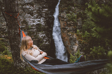 Wall Mural - Woman enjoying waterfall view lying in hammock in forest travel lifestyle outdoor with camping gear summer vacations girl hiking in Norway eco tourism adventure trip in the wild