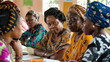 Several african women are seated around a table, engaged in conversation and possibly sharing a meal or working together