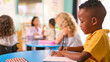 © Monkey Business - Male Primary Or Elementary School Student At Desk In Multi-Cultural Class With Teacher In Background