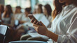 © MP Studio - Person's hand holding a smartphone with a blurred background of seated people.