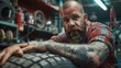 A bearded and tattooed technician balances an automobile wheel at a workshop. Generative Ai