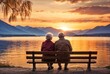Rear view of an elderly couple sitting on a bench looking at the lake and mountains in the amazing color sunset