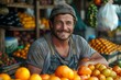 A smiling man with facial stubble leans on a market stall filled with citrus fruits, conveying approachability