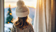 Blonde toddler in beanie waits at window for Santa, embodying innocence and anticipation