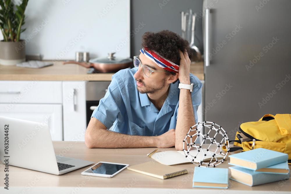 Male student studying at table in kitchen