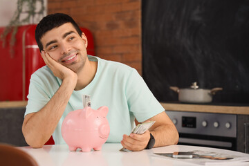 Wall Mural - Happy young man with money and piggy bank in kitchen