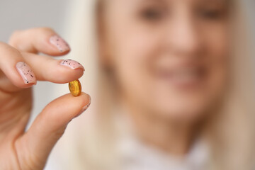 Wall Mural - Mature woman holding fish oil capsule at home, closeup