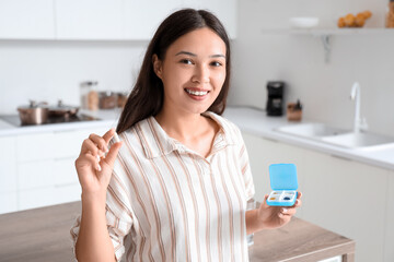 Poster - Young Asian woman pill organizer with pills in kitchen