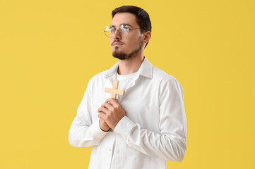 Wall Mural - Young man with wooden cross praying on yellow background