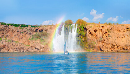 Wall Mural - Lonely yacht sailing in the Mediterranean sea with amazing rainbow - Powerful Duden waterfall with rainbow, a water stream breaks from a high cliff - Antalya, Turkey