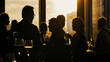 Silhouetted profiles of elegantly dressed people at a sophisticated social event at sunset.
