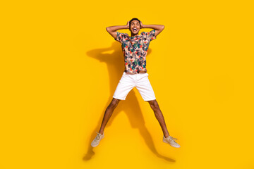Wall Mural - Full length photo of cheerful impressed man wear print t-shirt jumping high arms hands head isolated yellow color background