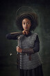 © master1305 - Brave young African woman, medieval warrior in chainmail armor with halo-like rings above head leaning sword on dark green vintage background. Concept of history, femininity, comparison of eras